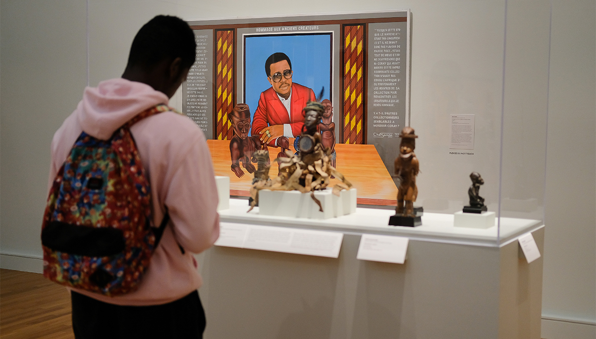 Student visitor stands in front of African Art exhibition with small wooden statues