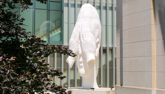 A white sculpture of a human head with hands covering its eyes