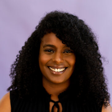 a woman poses for a headshot against a purple background