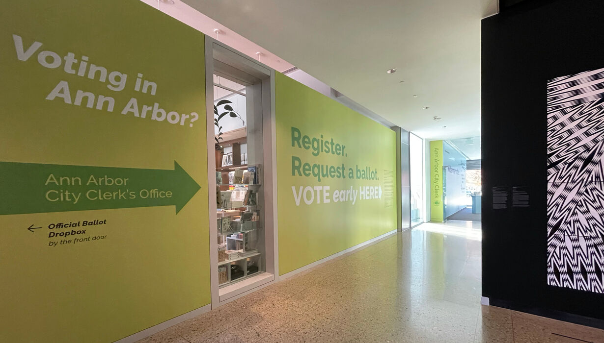 A bright green wall reads "Register. Request a ballot. Vote Early Here"