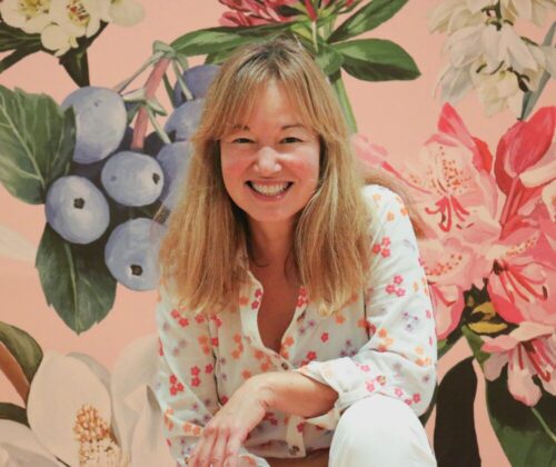 Philippa crouching and smiling in front of a vibrant floral backdrop.