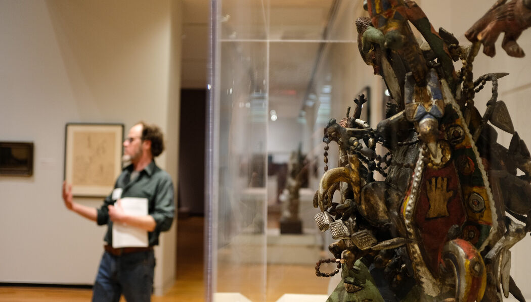 A small group of people stand around and discuss art in a gallery space with a sculptural piece is in the foreground.