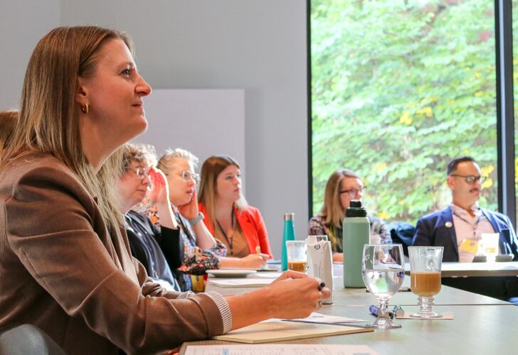 Attendees listening attentively at a conference table during a business meeting, with a scenic window view in the background.