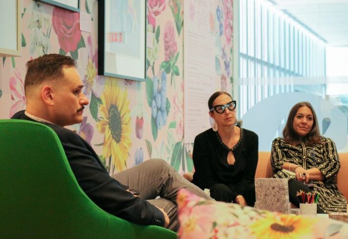 Three professionals seated in a vibrant meeting room with floral wallpapers, discussing ideas.