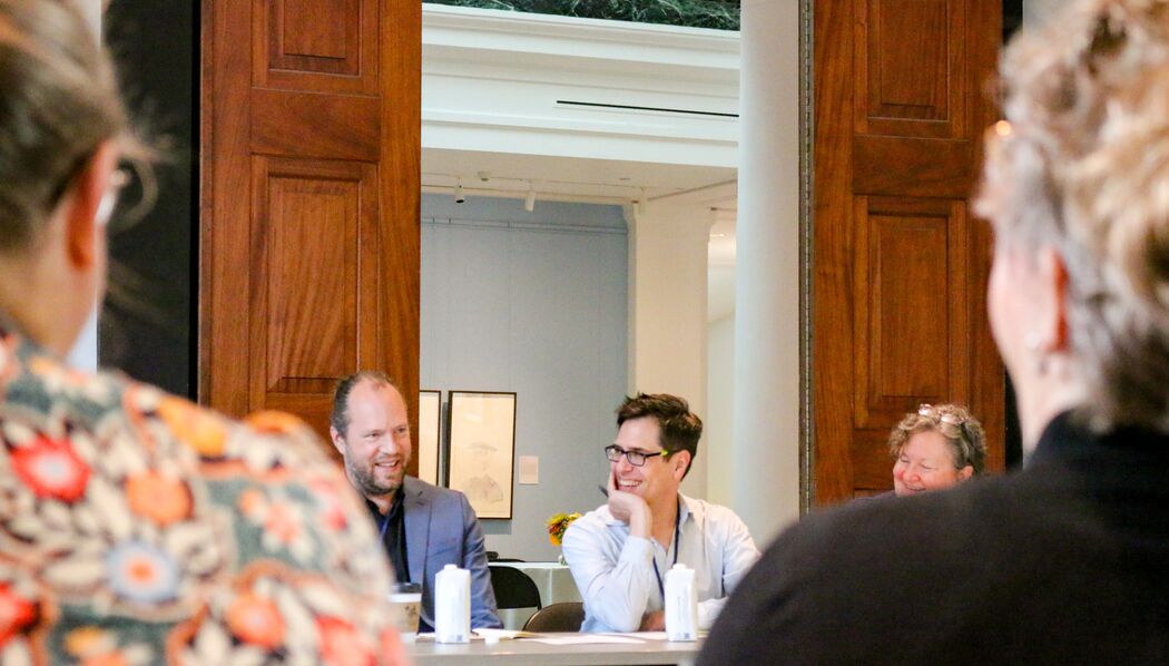 People seated at a conference table engaged in a discussion, with one person smiling broadly.