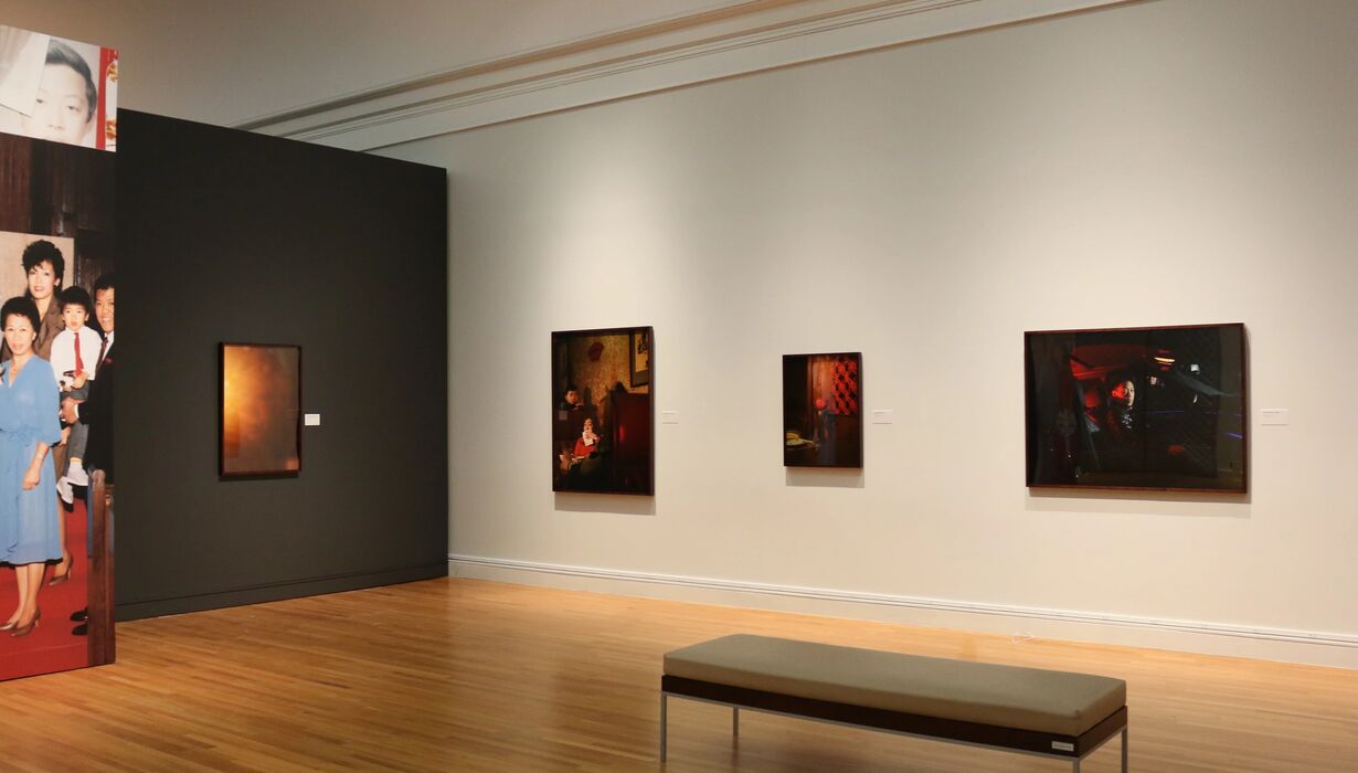 Interior of an art gallery displaying various photographs on the walls, with a bench centered in the foreground for viewers.