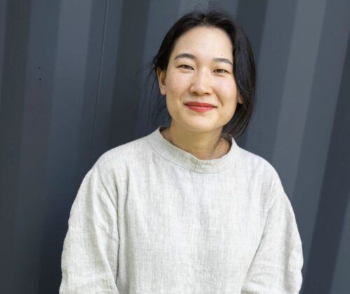 A woman sits for a portrait. She is seated in front of a grey background.