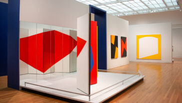 Installation view of a geometric abstract art exhibit featuring red and white panels arranged in a dynamic composition, displayed in a modern gallery setting.