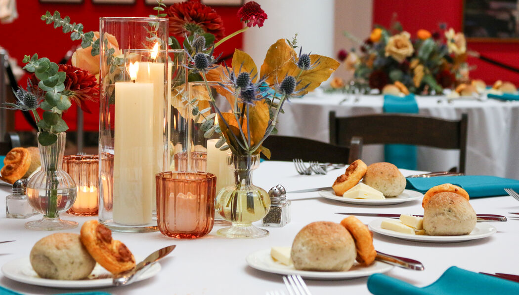 Elegant event setup in an art gallery with round tables covered in turquoise tablecloths and decorated with floral centerpieces.