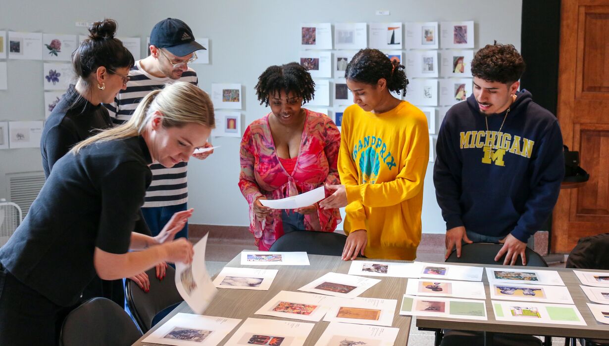 Five individuals collaborate around a table, examining and discussing various photographs and documents.