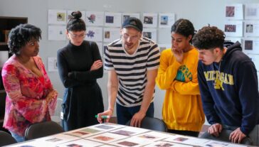 Six individuals collaborate around a table, examining and discussing various photographs and documents.