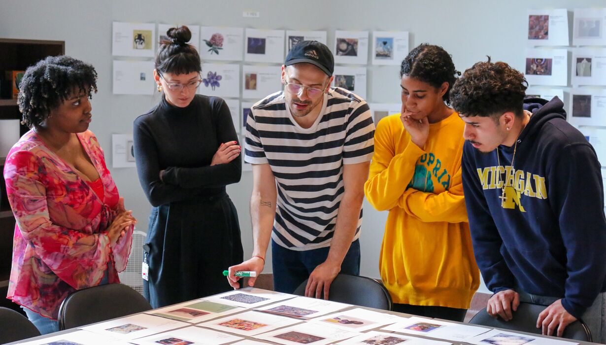 Six individuals collaborate around a table, examining and discussing various photographs and documents.