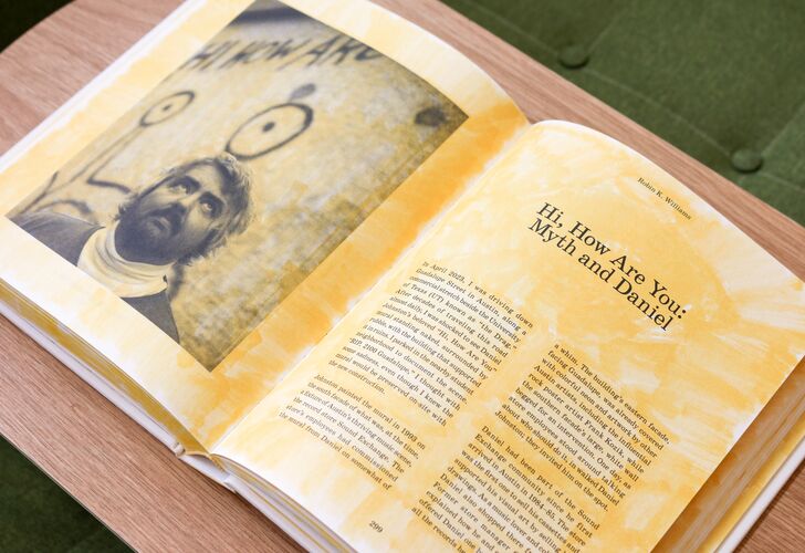 An open book on a green surface featuring a photograph of musician Daniel Johnston on the left page, and text titled "Hi, How Are You? Myth and Daniel Johnston" on the right page.