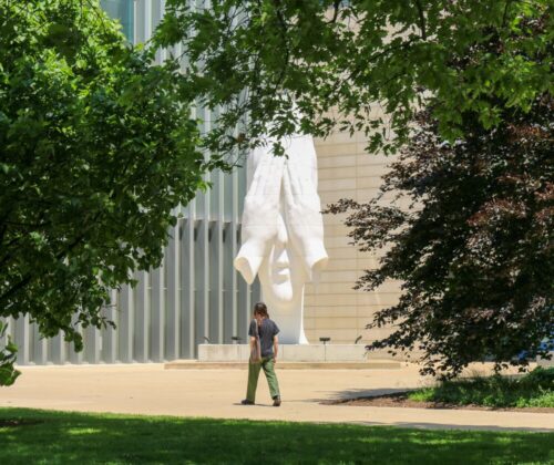 A person walking by Jaume Plensa's "Behind Our Wall" Statue.