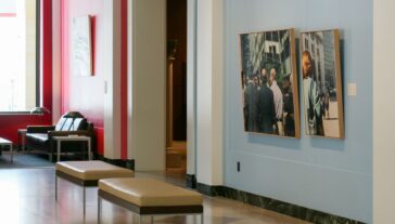 Interior of a modern art gallery featuring a series of framed photographs on light blue walls, with stylish seating areas. The setting is calm and spacious.