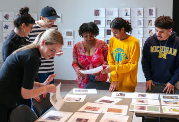 student curators gather around a table with prints of artwork surrounding them
