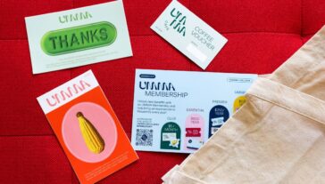 Assorted UMMA (University of Michigan Museum of Art) membership materials including cards and informational brochures on a red background next to a beige tote bag.