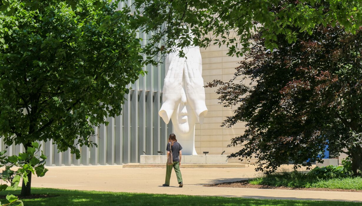 A person walking by Jaume Plensa's "Behind Our Wall" Statue.