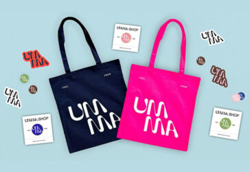 Two UMMA tote bags, one navy and one pink, surrounded by a variety of multi-colored UMMA logo stickers and pins.