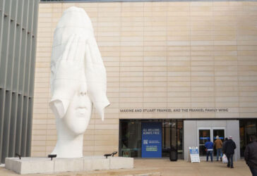 A large white sculpture of a head stands near a building entrance