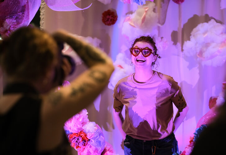 A photographer takes a photograph of people standing inside a large heart made out of paper flowers