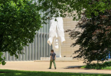 A person walking by Jaume Plensa's "Behind Our Wall" Statue.