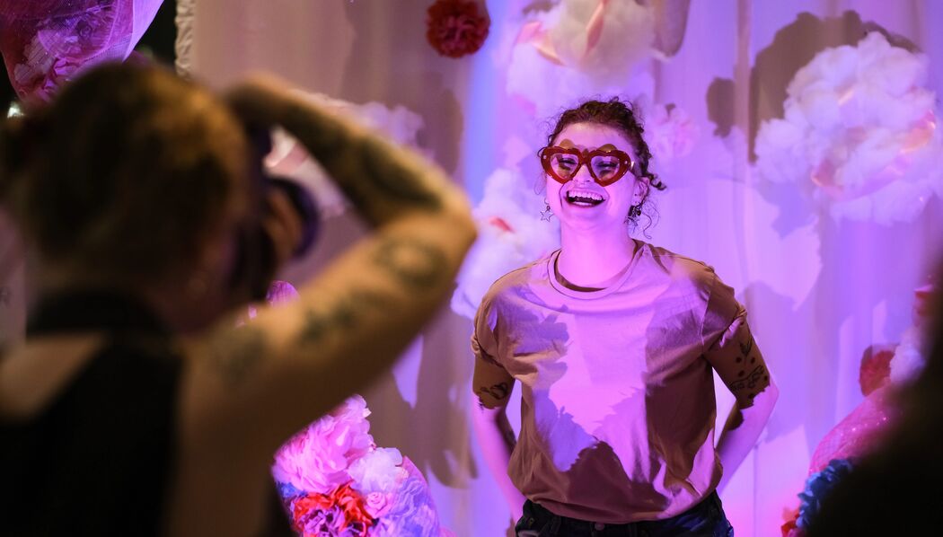 A photographer takes a photograph of people standing inside a large heart made out of paper flowers