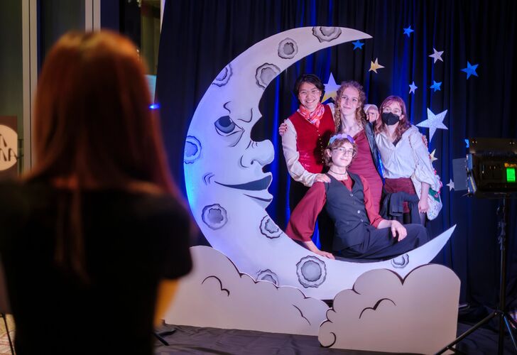 Group of people posing with a crescent moon prop at a themed event