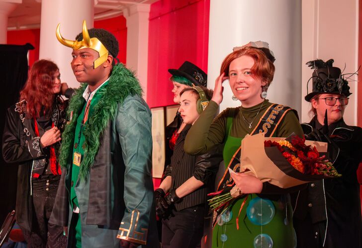 A group of people in costume at a themed event, featuring individuals dressed as a character with a horned helmet and another with a green outfit adorned with bubbles, among others in various imaginative outfits.