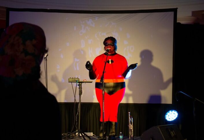 Person dressed as Mr. Incredible singing into a microphone at an event.