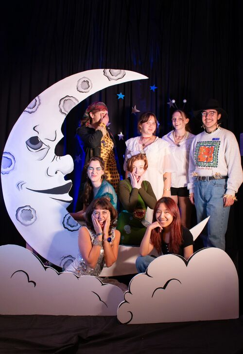 Group of people posing with a crescent moon prop at a themed event