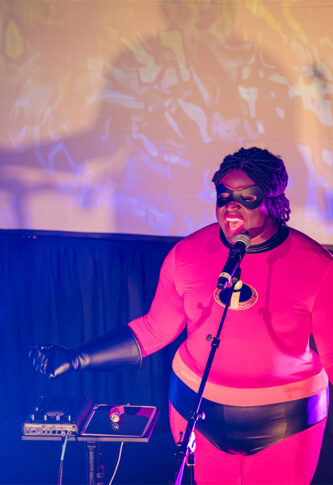 Person dressed as Mr. Incredible singing into a microphone at an event.