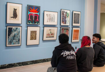 Three people sitting on a bench in an art gallery with vibrant red and blue walls and colorful artwork displayed.
