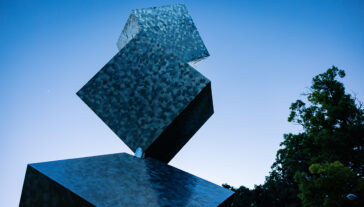3 Cubes in a Seven Axis Relationship reflects the dark blue sky as the sun sets on North Campus