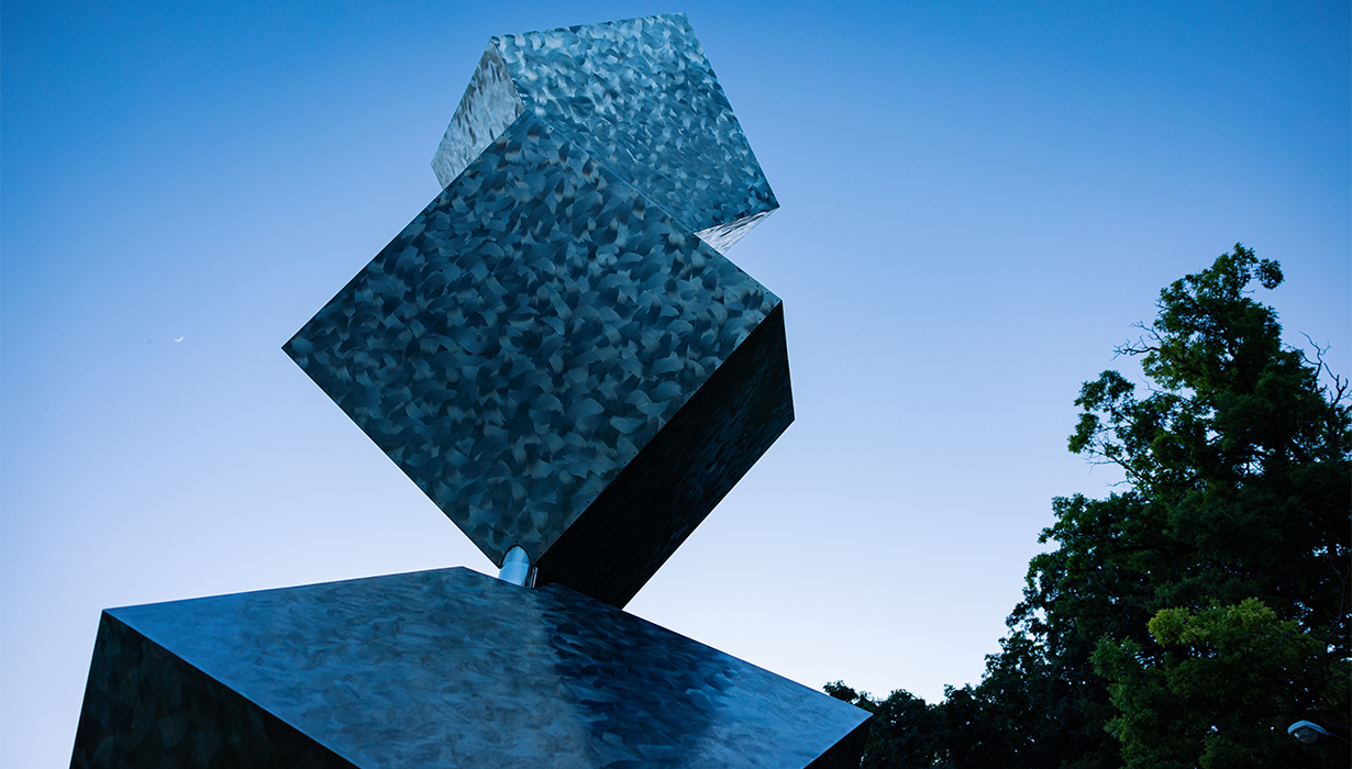 3 Cubes in a Seven Axis Relationship reflects the dark blue sky as the sun sets on North Campus