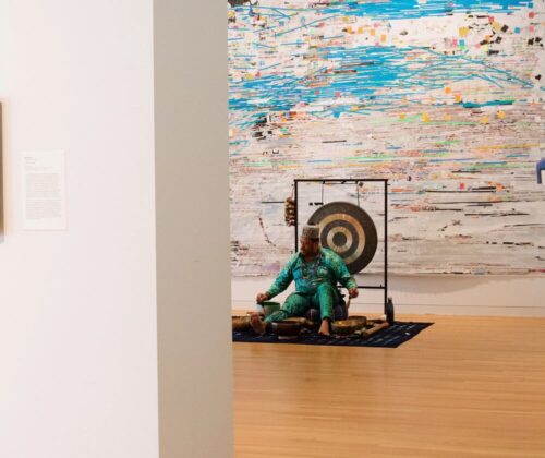 During 'Study Days' at UMMA from April 26-28, 2024, a meditation facilitator sits on a blanket in the middle of a large exhibition space, leading a sound bath meditation session.