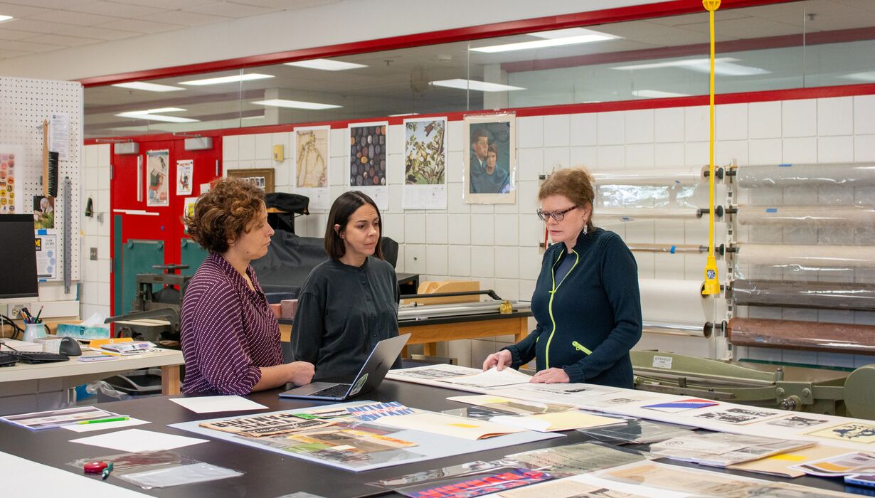 Three people discussing work over a laptop and printed materials.