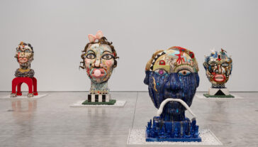 Image of a gallery space with white walls and grey floor with 4 large abstract bust sculptures.