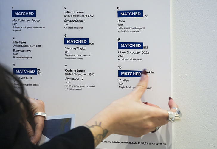 Someone placing a 'Matched' sticker on the lists of artworks on view.