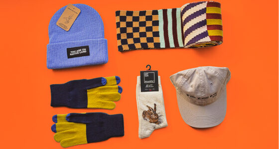 Flat lay of colorful knit garments and wearable accessories on an orange background.