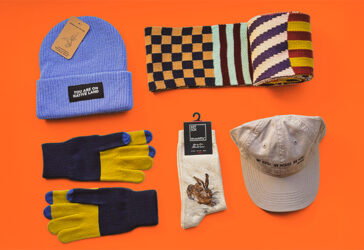 Flat lay of colorful knit garments and wearable accessories on an orange background.