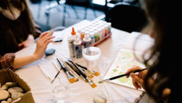 a hand holds a paintbrush above a messy art-making table