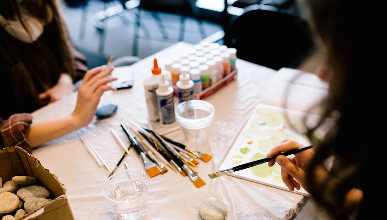a hand holds a paintbrush above a messy art-making table