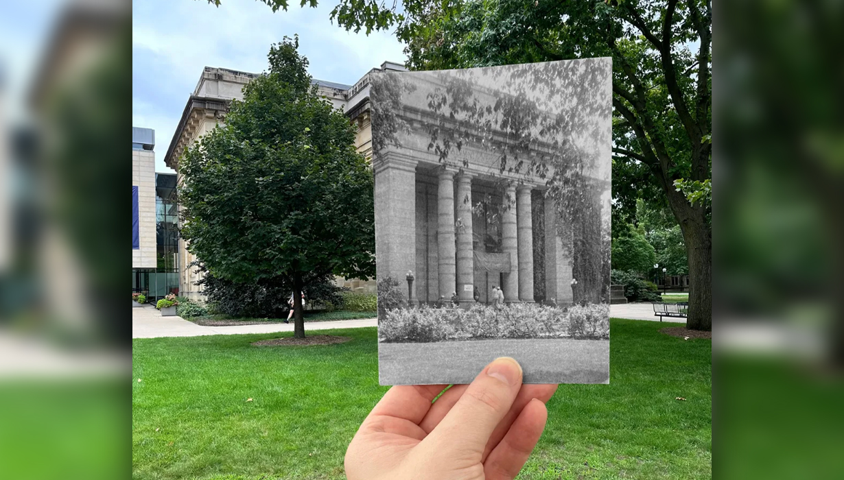 A hand holds an old black and white photo infront of the same spot in present day